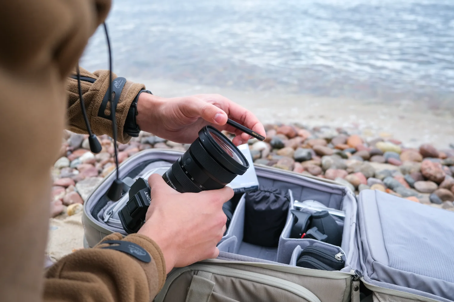 Marumi PRIME II Lens Protect – ochrona obiektywu w nowym wydaniu zdjęcie przedstawiające filtr Marumi Prime II Lens Protect podczas przykręcania na gwint obiektywu przy plecaku fotograficznym