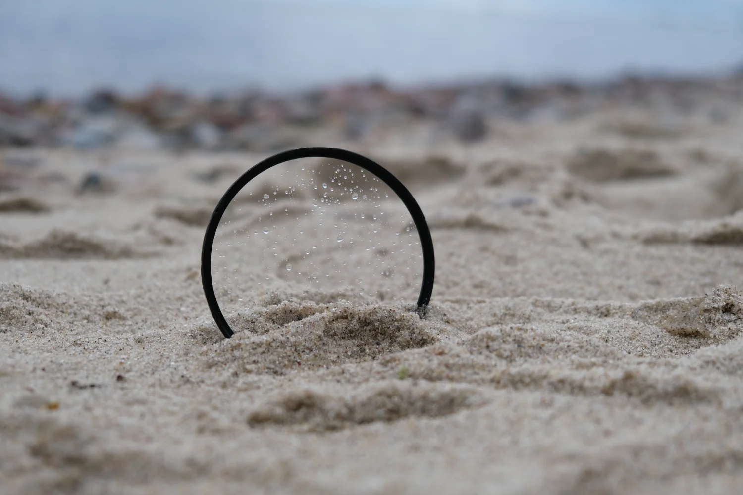 Marumi PRIME II Lens Protect – ochrona obiektywu w nowym wydaniu zdjęcie przedstawiające filtr Marumi Prime II Lens Protect na piasku na plaży z kroplami wody na powierzchni filtra