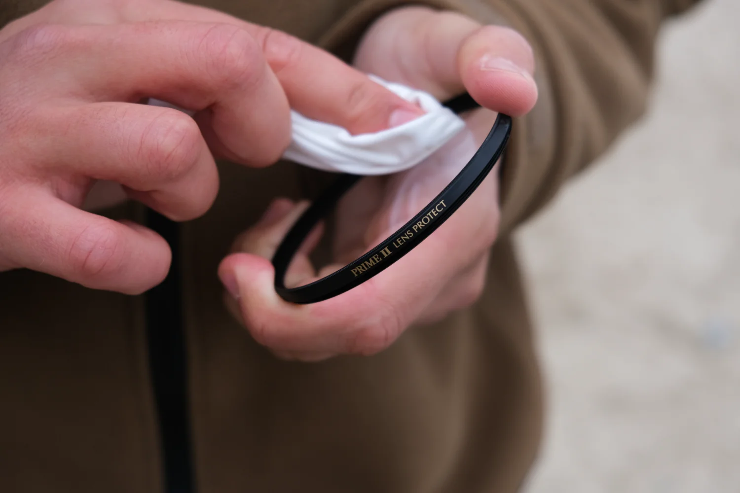 Marumi PRIME II Lens Protect – ochrona obiektywu w nowym wydaniu zdjęcie przedstawiając palce fotografa czyszczącego powierzchnię filtra Marumi Prime II Lens Protect