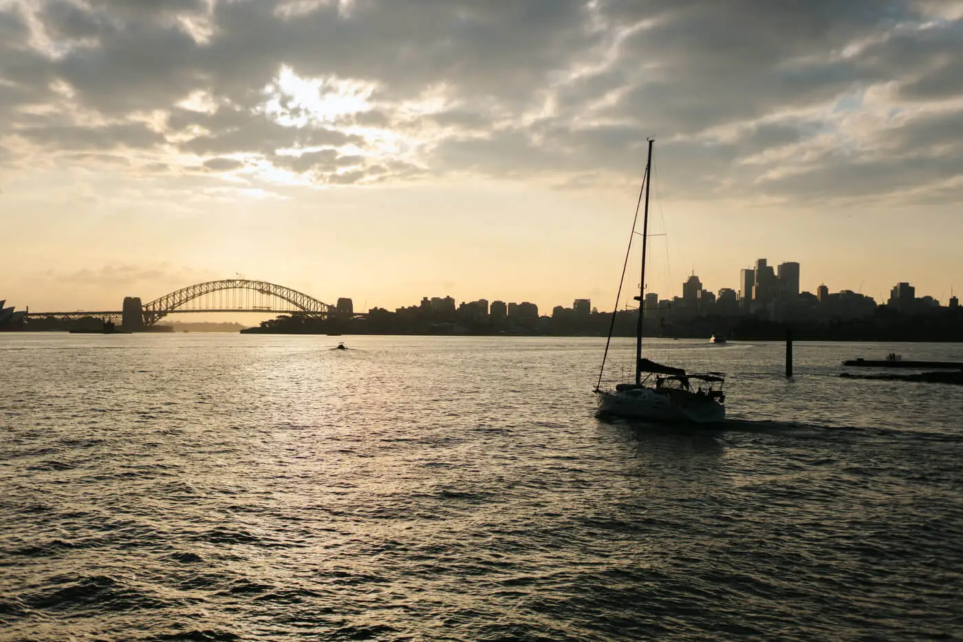 Żaglówka na tle mostu i panoramy Sydney w wieczornym świetle
